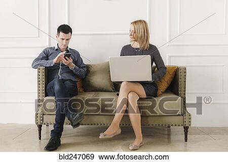 Stock Photo - Middle Eastern couple sitting on sofa using technology. Fotosearch