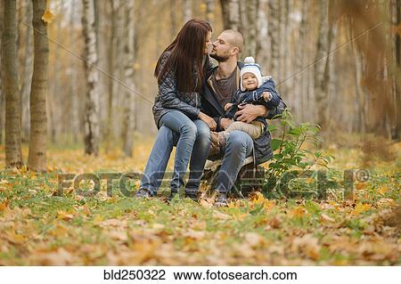 Stock Image - Middle Eastern couple sitting on tree stump with baby son in autumn. Fotosearch