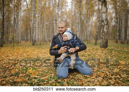 Stock Image - Middle Eastern father kneeling in park with baby son in autumn. Fotosearch
