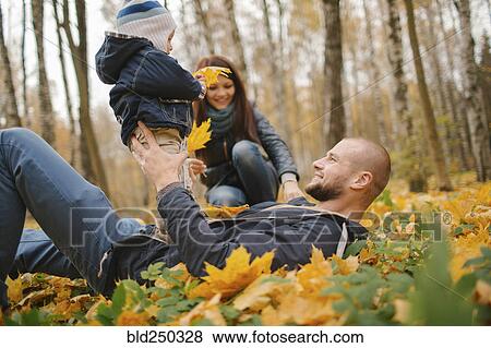 Stock Photo - Middle Eastern father laying in autumn leaves holding baby son. Fotosearch