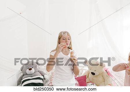 Stock Image - Middle Eastern girl blowing bubbles in bedroom. Fotosearch