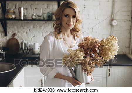 Stock Image - Middle Eastern holding kettle of flowers in domestic kitchen. Fotosearch
