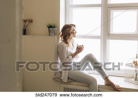 Middle Eastern woman sitting in window sill drinking coffee View Large Photo Image Stock Photo - Middle Eastern woman sitting in window sill drinking coffee. Fotosearch