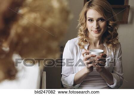 Stock Image - Middle Eastern woman sitting near window drinking coffee. Fotosearch