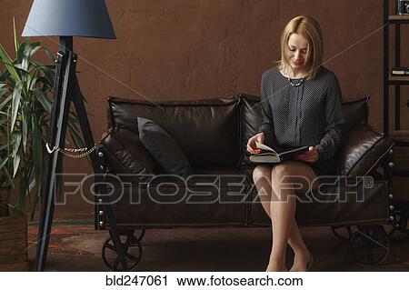Stock Image - Middle Eastern woman sitting on sofa reading book. Fotosearch