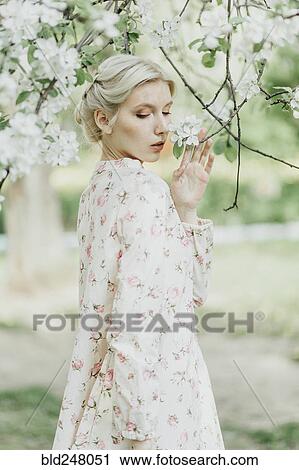Stock Image - Middle Eastern woman smelling flowers on tree. Fotosearch