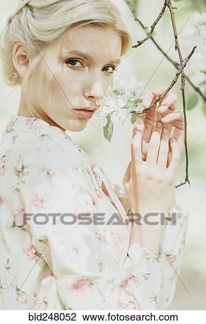 Stock Image - Middle Eastern woman smelling flowers on tree. Fotosearch