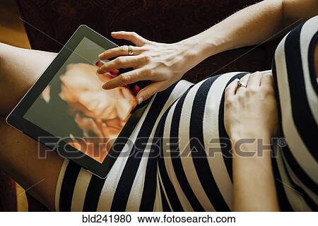Stock Image - Midsection of pregnant Caucasian woman using digital tablet. Fotosearch