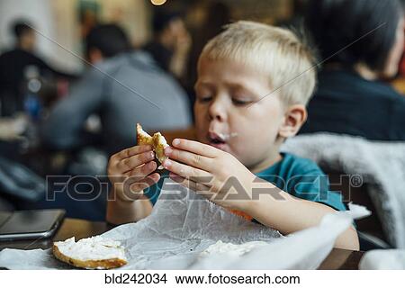 Mixed Race boy eating messy bagel in restaurant View Large Photo Image Picture - Mixed Race boy eating messy bagel in restaurant. Fotosearch
