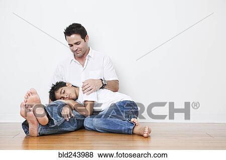Stock Photo - Mixed Race boy napping in lap of father on floor. Fotosearch
