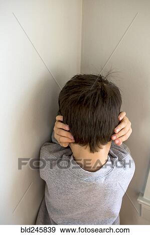 Stock Photo - Mixed Race boy standing in corner covering ears. Fotosearch