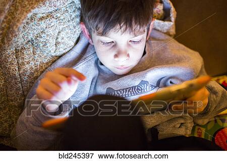 Stock Photo - Mixed Race boy using digital tablet at night. Fotosearch
