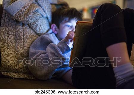 Stock Photograph - Mixed Race boy using digital tablet at night. Fotosearch