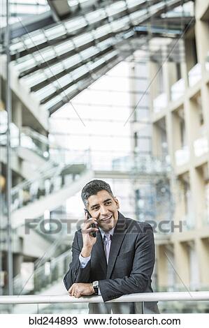 Mixed Race businessman leaning on railing in lobby talking on cell phone View Large Photo Image Stock Image - Mixed Race businessman leaning on railing in lobby talking on cell phone. Fotosearch