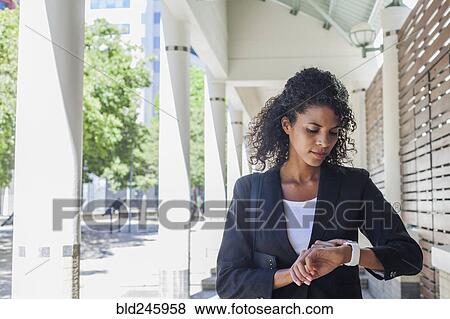 Stock Photo - Mixed Race businesswoman checking the time on wristwatch. Fotosearch