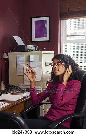 Mixed Race businesswoman listening to headphones in office View Large Photo Image Stock Image - Mixed Race businesswoman listening to headphones in office. Fotosearch