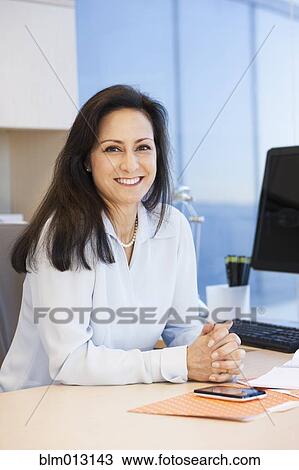 Stock Image - Mixed race businesswoman sitting at desk. Fotosearch