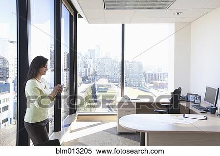 Stock Photography - Mixed race businesswoman text messaging on cell phone in office. Fotosearch