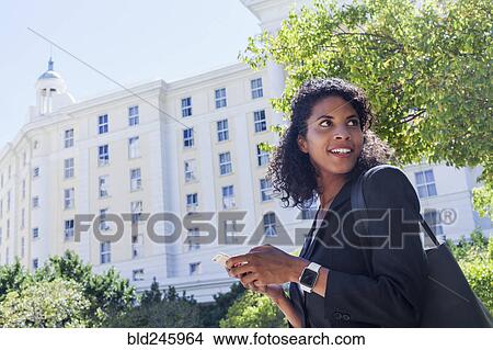 Picture - Mixed Race businesswoman texting on cell phone outdoors. Fotosearch