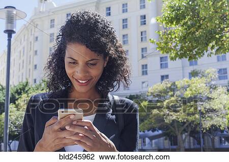 Stock Image - Mixed Race businesswoman texting on cell phone outdoors. Fotosearch