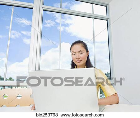 Stock Photo - Mixed Race businesswoman using laptop near window. Fotosearch