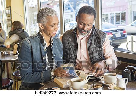 Stock Photo - Mixed Race couple reading travel guidebook in coffee shop. Fotosearch