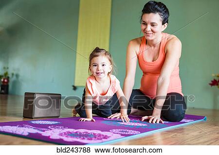 Stock Photo - Mixed Race expectant mother and daughter on exercise mat. Fotosearch