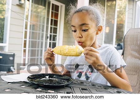 Stock Image - Mixed Race girl eating corn on the cob outdoors. Fotosearch