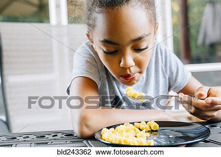 Stock Image - Mixed Race girl eating food with fork. Fotosearch