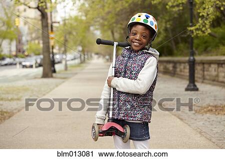 Stock Image - Mixed race girl holding push scooter on sidewalk. Fotosearch