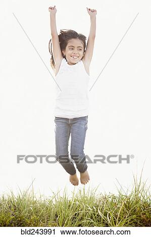 Stock Image - Mixed Race girl jumping for joy in grass. Fotosearch