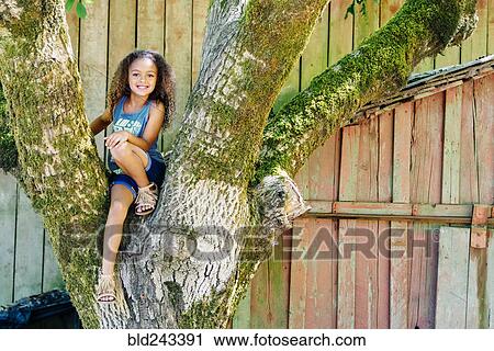 Stock Image - Mixed Race girl sitting in tree. Fotosearch