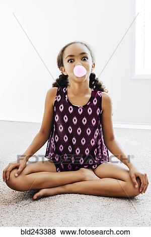 Stock Photo - Mixed Race girl sitting on floor blowing bubble with gum. Fotosearch