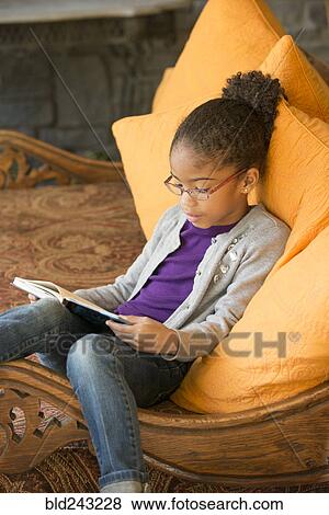 Mixed Race girl sitting on sofa reading book View Large Photo Image Stock Photo - Mixed Race girl sitting on sofa reading book. Fotosearch