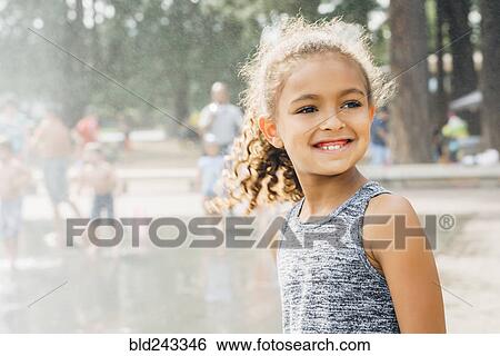 Stock Photograph - Mixed Race girl smiling in park near fountain. Fotosearch
