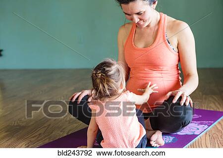 Stock Image - Mixed Race girl touching belly of expectant mother on exercise mat. Fotosearch