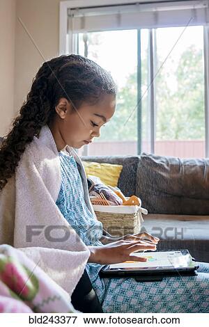 Stock Photo - Mixed Race girl using digital tablet on sofa. Fotosearch