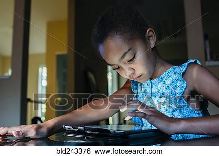 Stock Photograph - Mixed Race girl using digital tablet on table at night. Fotosearch