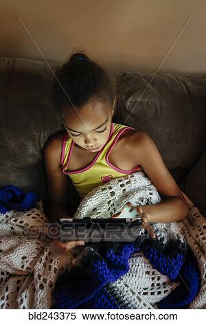Stock Photography - Mixed Race girl using digital tablet on sofa at night. Fotosearch