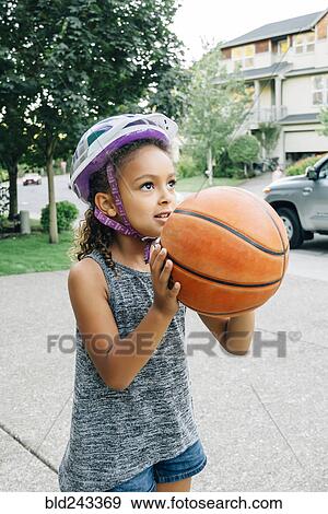 Stock Photo - Mixed Race girl wearing helmet playing basketball in driveway. Fotosearch