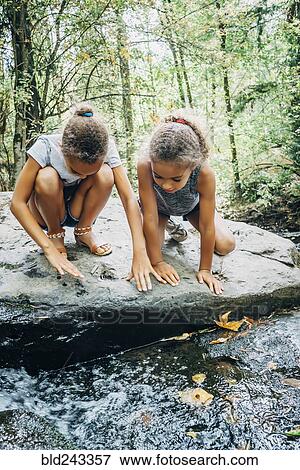 Stock Photo - Mixed Race girls kneeling on rock looking at stream. Fotosearch