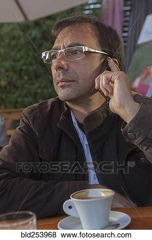 Stock Photo - Mixed Race man at cafe talking on cell phone. Fotosearch