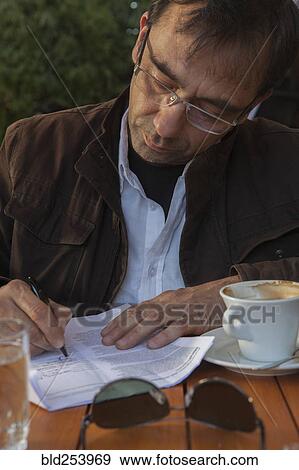 Stock Photo - Mixed Race man at cafe writing on paperwork. Fotosearch