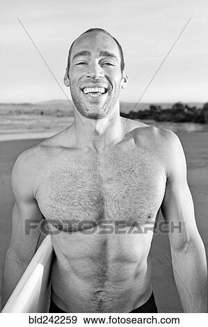 Stock Photo - Mixed race man carrying surfboard on beach. Fotosearch