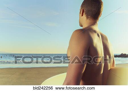 Stock Photograph - Mixed race man carrying surfboard on beach. Fotosearch