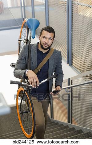 Stock Photography - Mixed Race man climbing staircase carrying bicycle. Fotosearch