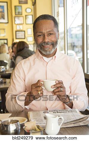 Stock Photo - Mixed Race man drinking coffee in coffee shop. Fotosearch