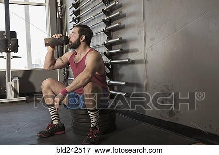 Stock Photo - Mixed Race man drinking from bottle in gymnasium. Fotosearch