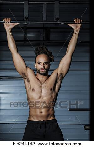 Stock Image - Mixed Race man holding bar in gymnasium. Fotosearch