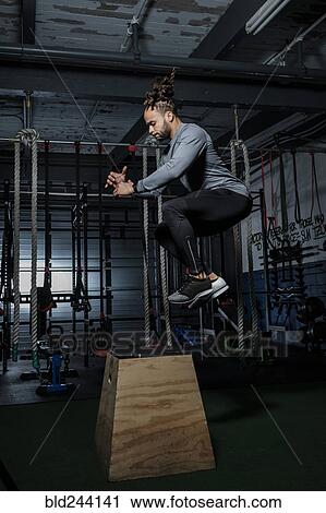 Stock Image - Mixed Race man jumping on wooden platform in gymnasium. Fotosearch